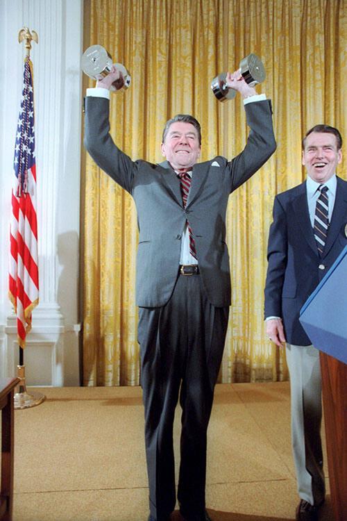 C6143-24, President Reagan lifting weights, with George Allen looking on, during a reception fo…